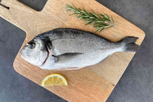 Frische ganze Dorade roh auf Holzbrett mit Rosmarin und Zitrone – ideal für mediterrane Fischgerichte